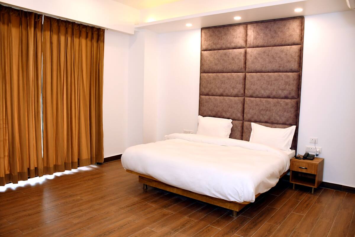 Une chambre à coucher moderne avec un grand lit, un plancher en bois, une tête de lit rembourrée et une table de chevet avec un téléphone.