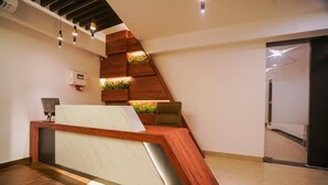 Un comptoir d’accueil avec un revêtement en bois, un espace salon avec des sièges rembourrés blancs et un jardin intégré agrémenté de plantes vertes.