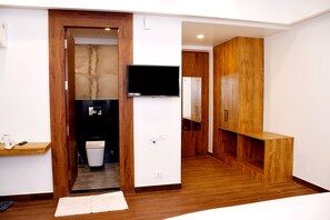 Quarto de hotel moderno com piso de madeira, um banco embutido, uma TV de tela plana na parede e uma pequena área de cozinha.