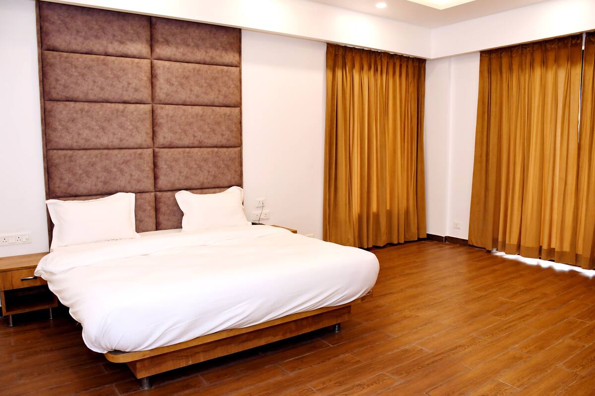 Une chambre moderne avec un grand lit, un plancher en bois et une tête de lit capitonnée.