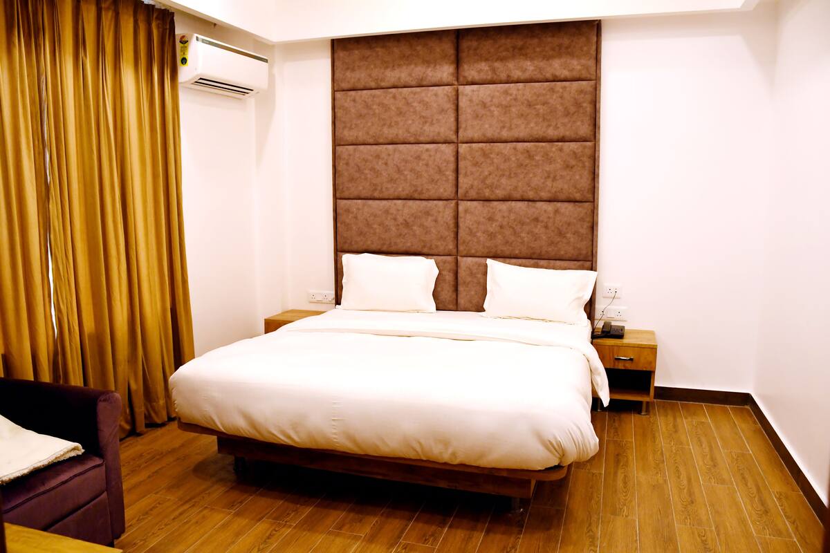 Une chambre d’hôtel avec un grand lit, une table de chevet en bois, une chaise et une fenêtre avec des rideaux.