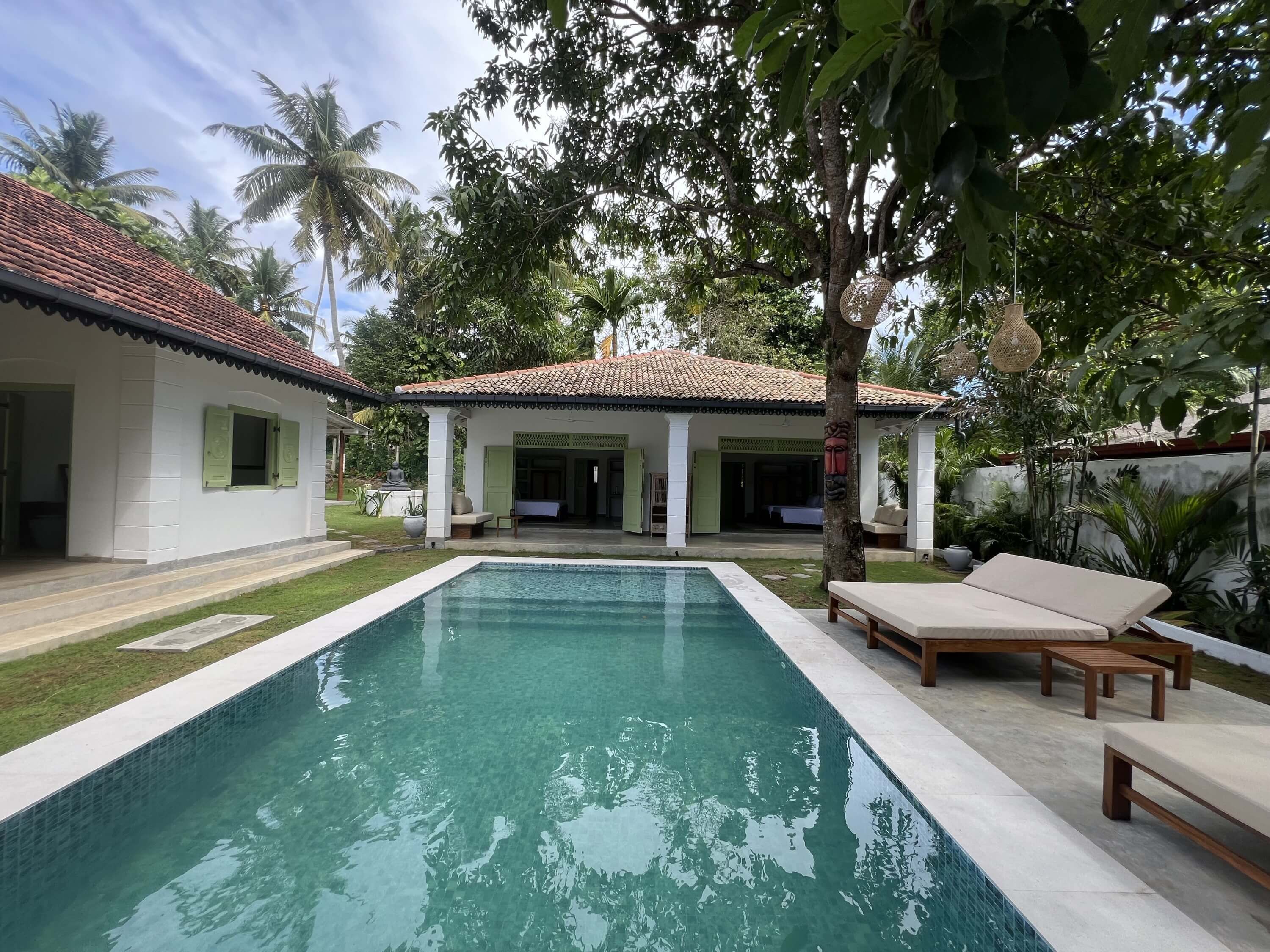 Une piscine avec une terrasse carrelée, un patio couvert et des chaises longues.