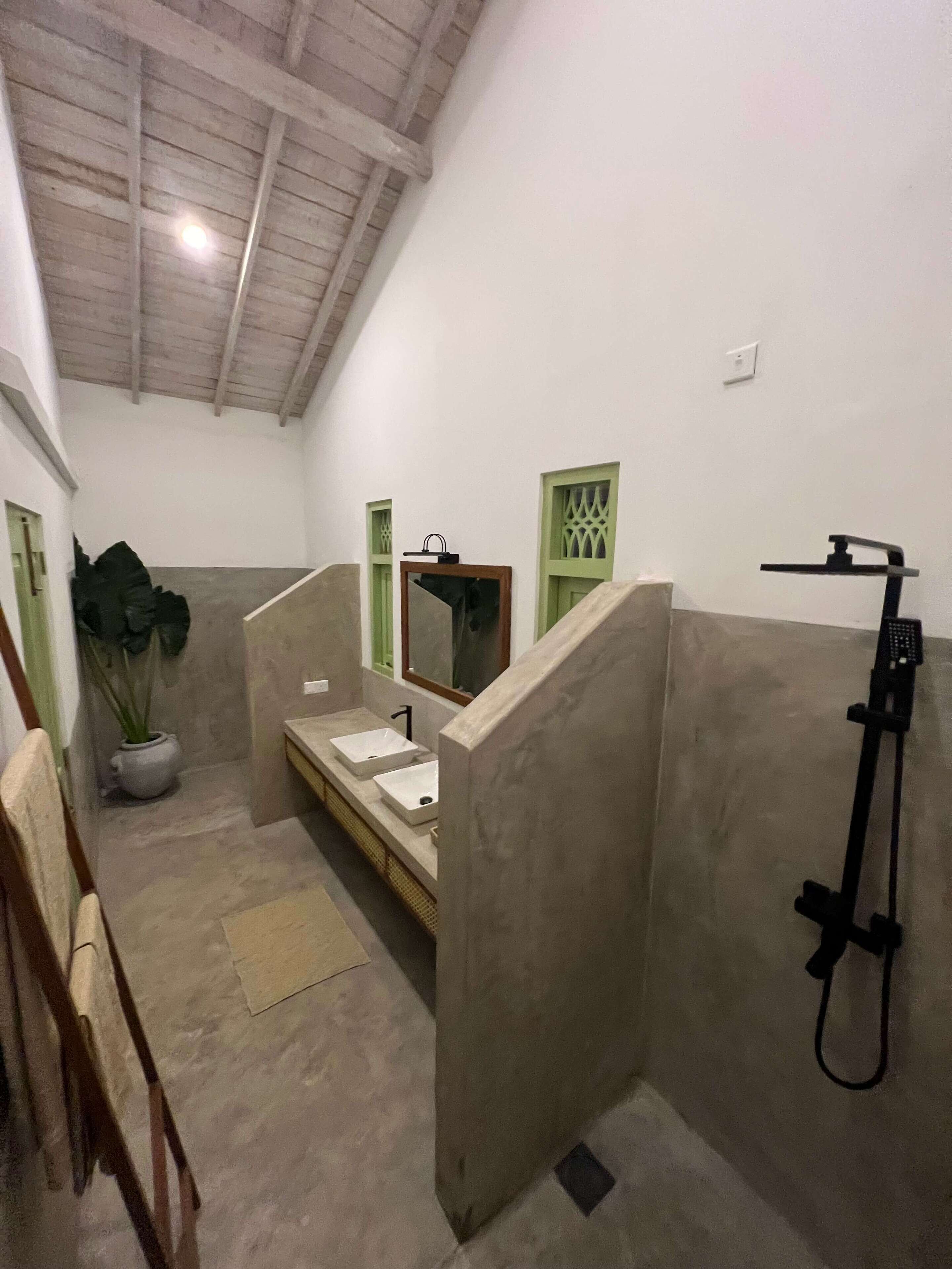 A bathroom with a shower, a sink, and a mirror. There is a potted plant and a chair.