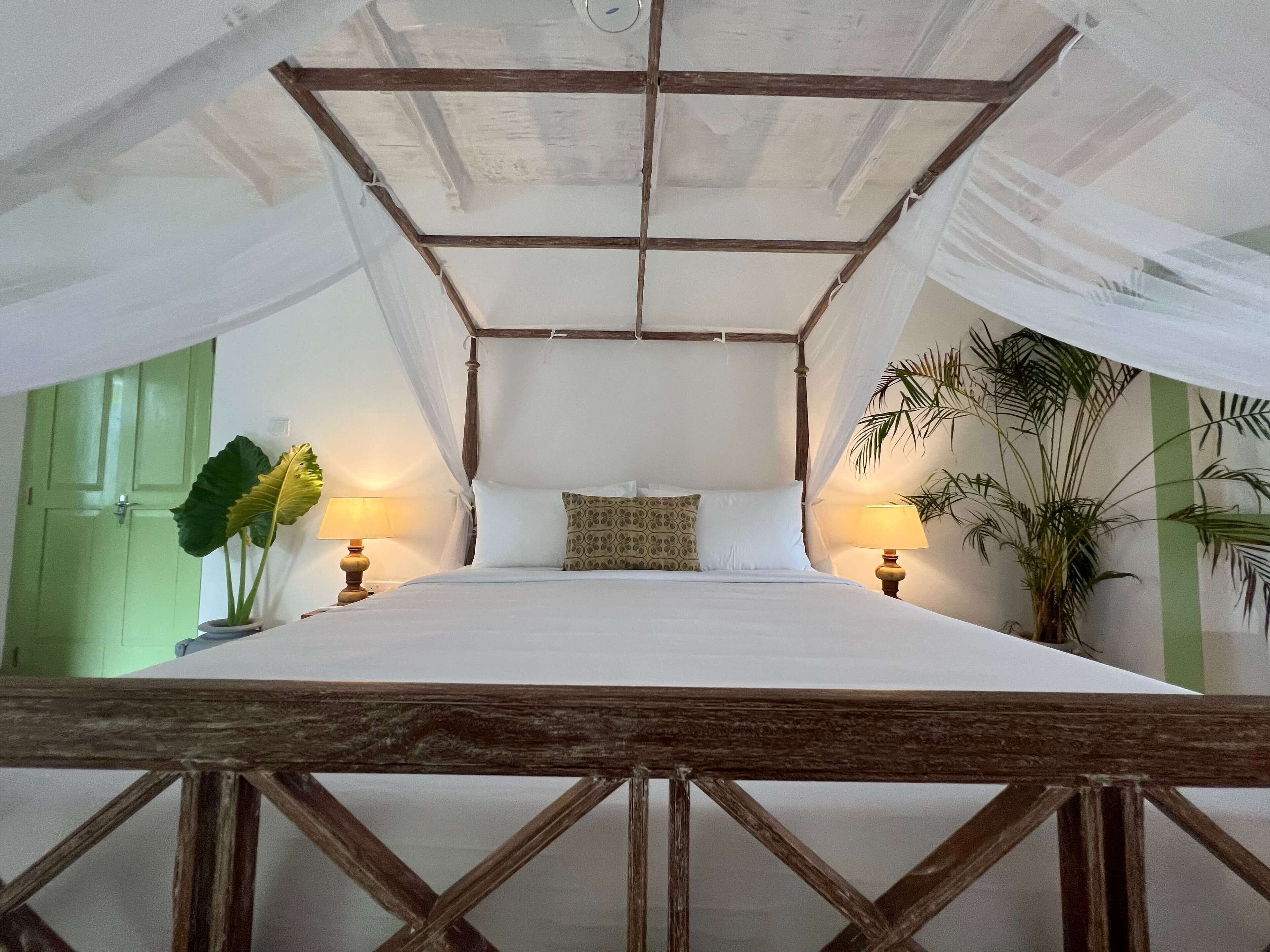 Una habitación con una cama, dos mesitas de noche y un dosel, con vistas al exterior.