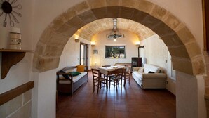 An interior with a stone archway, a dining area with a table and chairs, a sofa, and a window with natural light.