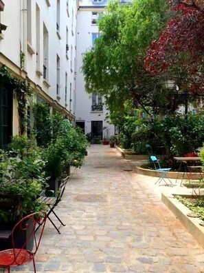 A narrow courtyard with stone flooring, potted plants, and outdoor seating. - Cocoon Bailly. Spacieux Studio Pigalle/montmartre (Paris)