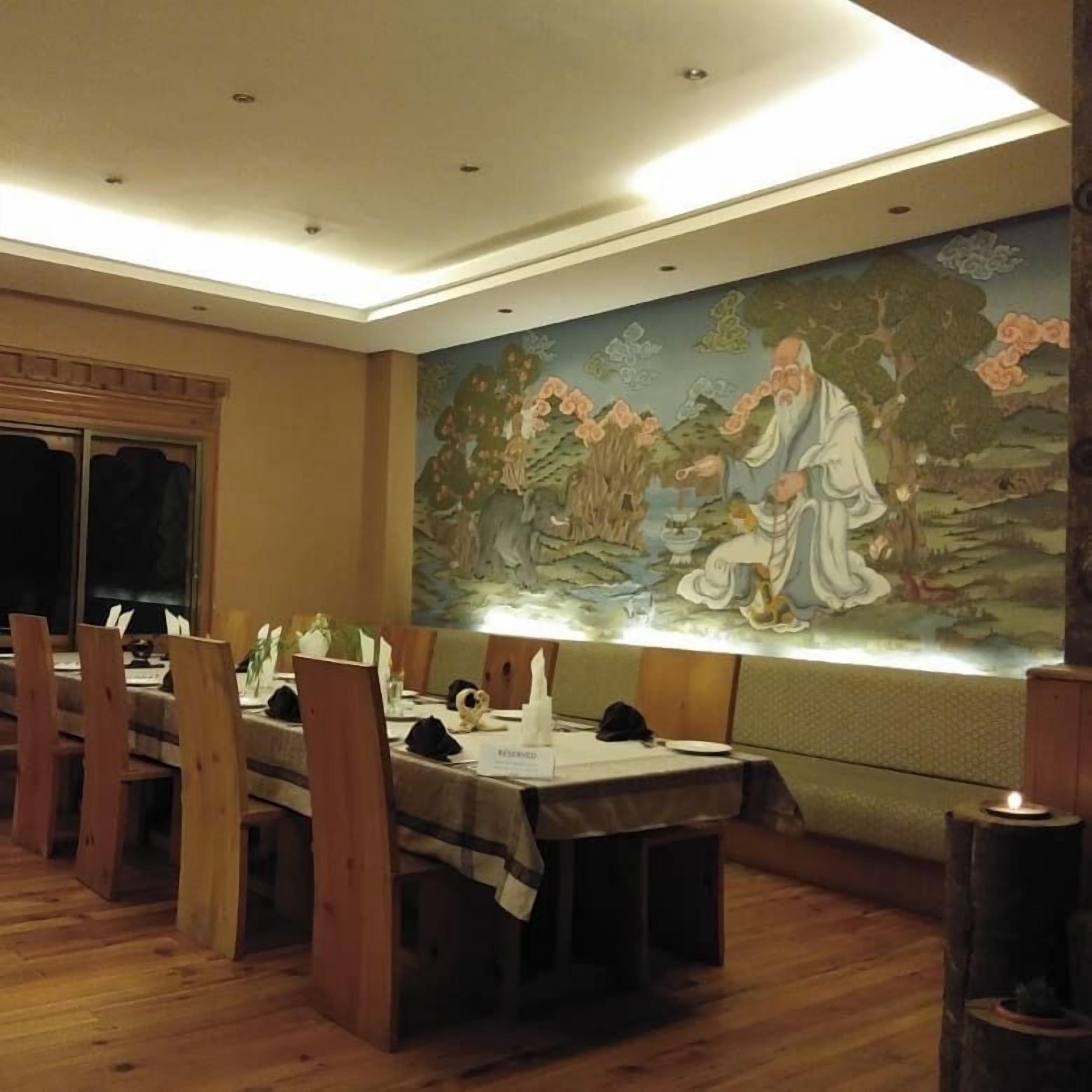 Ein Essbereich mit Holztischen und -stühlen, einem Wandgemälde und einer Decke mit Einbautenleuchten.