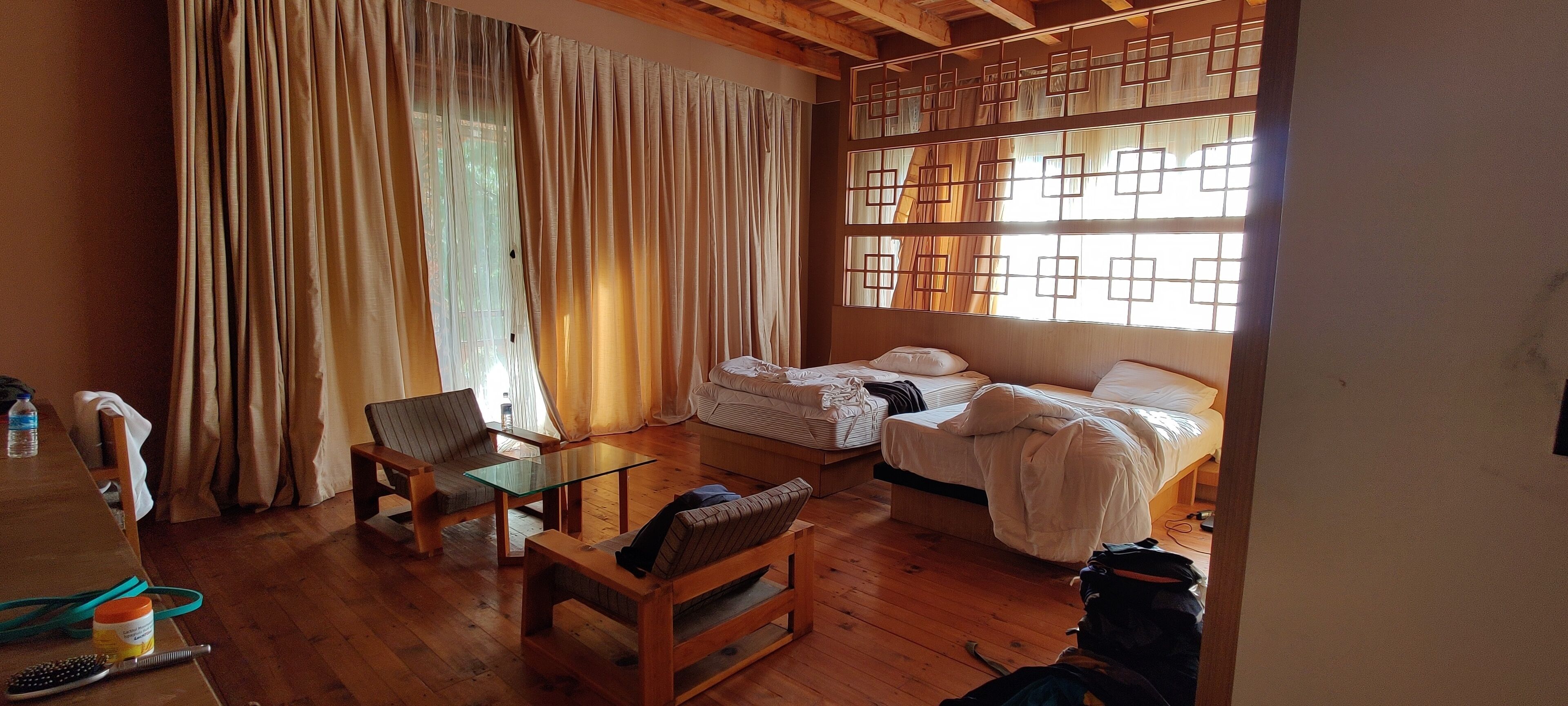 A room with a wooden floor, a bed with white bedding, a chair, a small table, and a window with curtains.