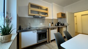 A modern kitchen with a built-in oven, a sink, and wooden cabinets. There is a dining table with chairs and a potted plant on the counter. - Dein Citynest - FeWo Meier (Bielefeld)