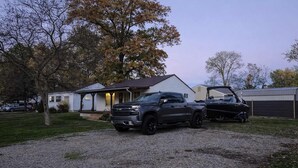 A gravel driveway with a dark-colored pickup truck and a boat parked in the driveway. - Homesmith Cottage|Hot Tub| Walk to Buckeye Lake (Buckeye Lake)