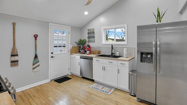 A modern kitchen with white cabinets, a stainless steel refrigerator, a ceiling fan, and a window with a view of the outdoors. - Homesmith Cottage|Hot Tub| Walk to Buckeye Lake (Buckeye Lake)
