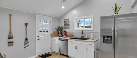 Una cocina moderna con gabinetes blancos, un refrigerador de acero inoxidable, un ventilador de techo y una ventana con vistas al exterior.