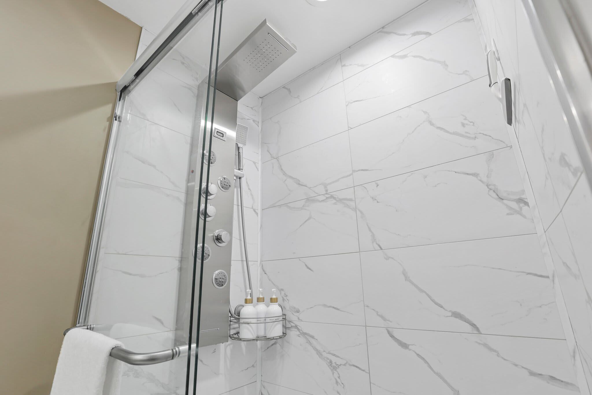A modern bathroom with a glass-enclosed shower, marble tiles, and a towel rack with bottles.