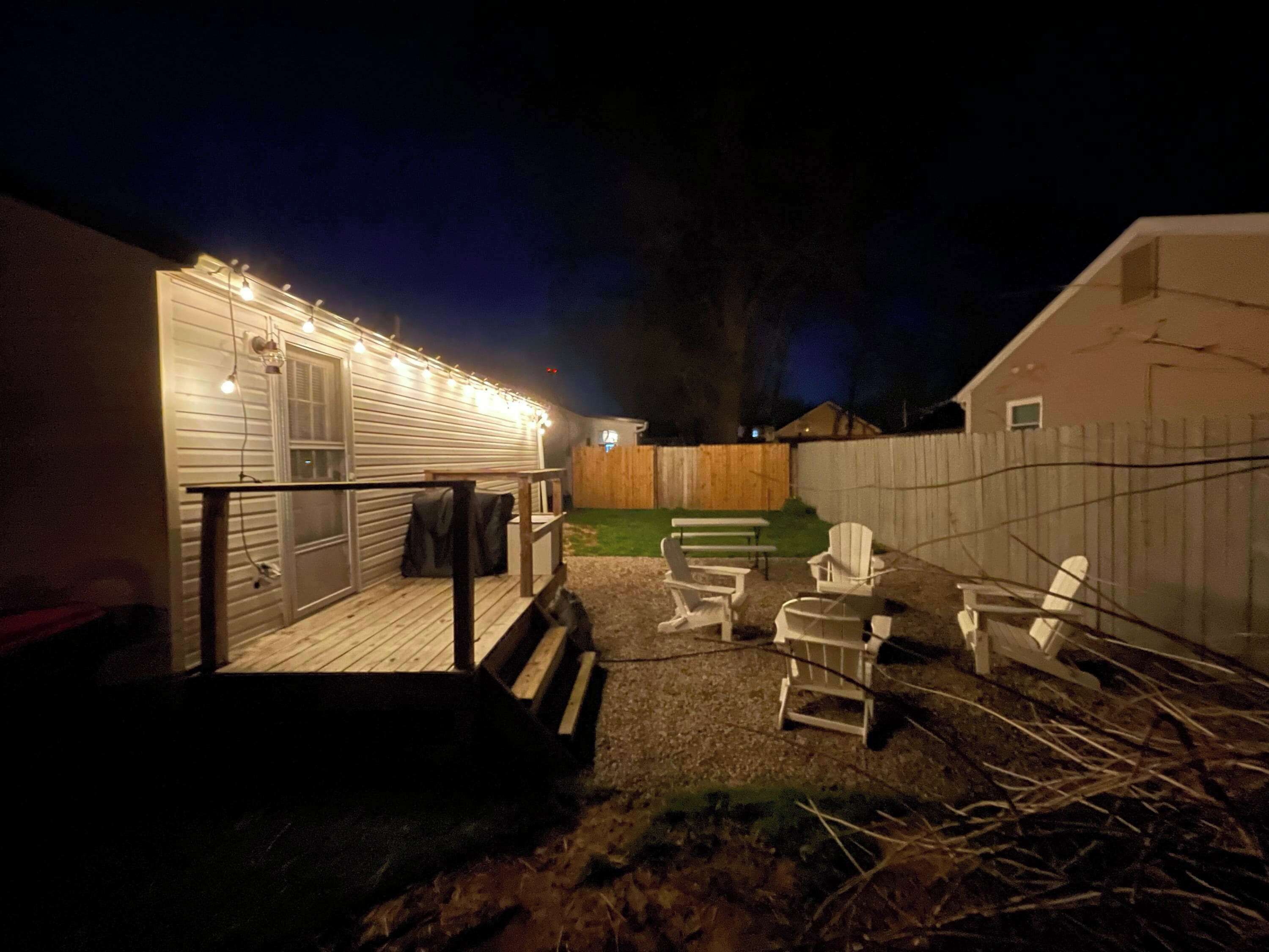 Een achtertuin met een houten terras, buitenmeubels en lichtslingers.