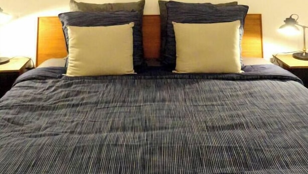 A bed with a striped bedspread, two pillows, and two wall-mounted paintings. - Nest Bailly. Superbe Studio Pigalle/montmartre (Paris)