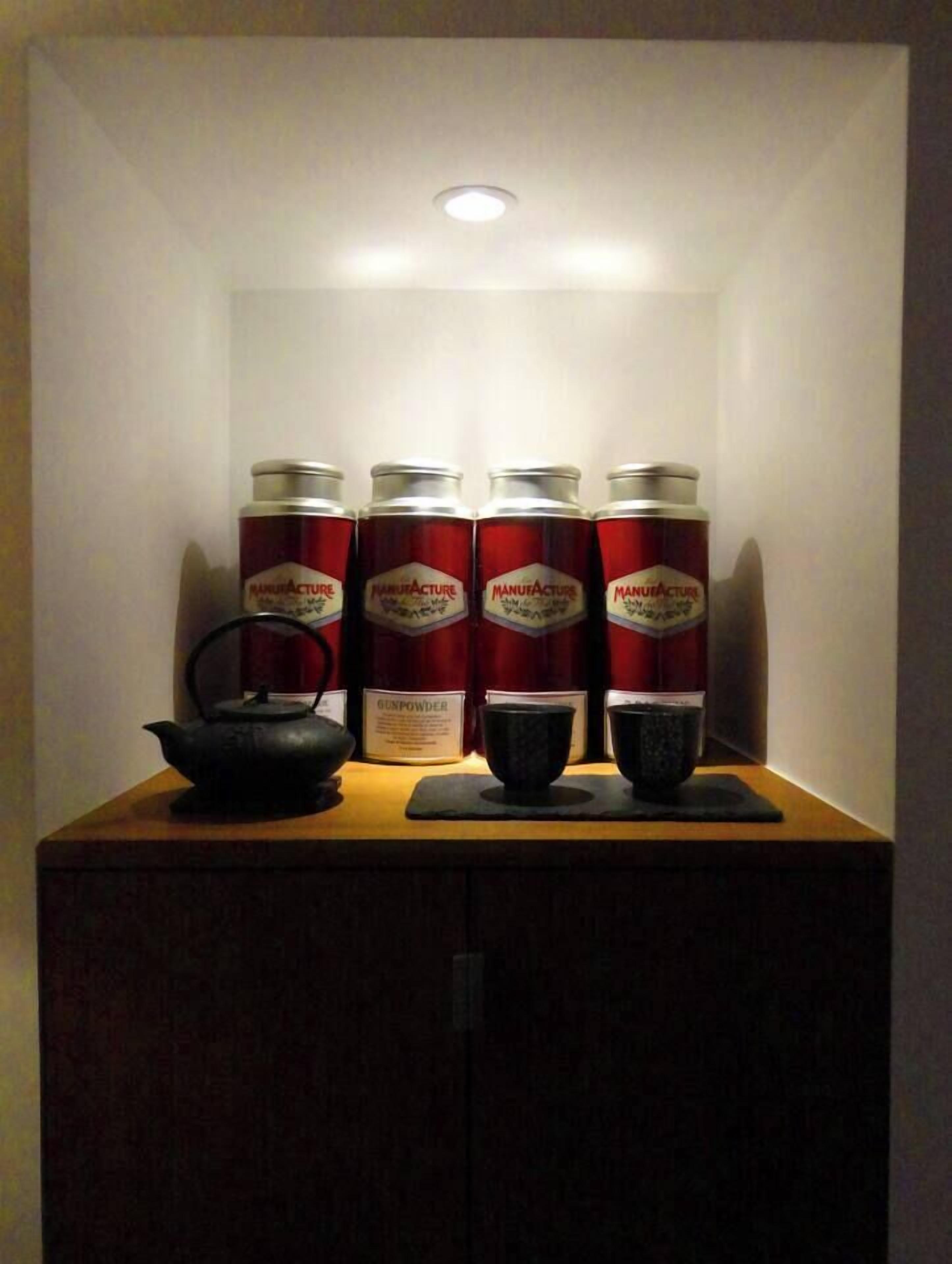 Un armario con cuatro latas rojas etiquetadas 'MANUFACTURER' y dos recipientes negros encima.