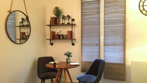 A room with a round table, two chairs, a mirror, and shelves with decorative items. - Nest Bailly. Superbe Studio Pigalle/montmartre (Paris)