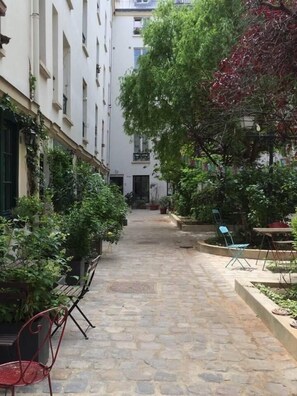 A narrow courtyard with stone flooring, potted plants, and outdoor seating. - Nest Bailly. Superbe Studio Pigalle/montmartre (Paris)