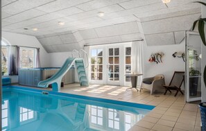 Una piscina interior con tobogán, una bañera de hidromasaje y una zona de estar con mesa y sillas.