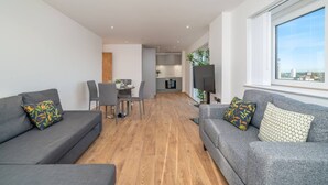 A modern living room with two grey sofas, a dining area, and a kitchen in the background. - Skyvillion - River View Mins To O2 & London Excel (London)