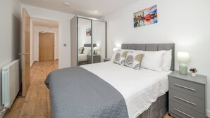 A bedroom with a bed, bedside tables, a wardrobe, and a painting on the wall. - Skyvillion - River View Mins To O2 & London Excel (London)