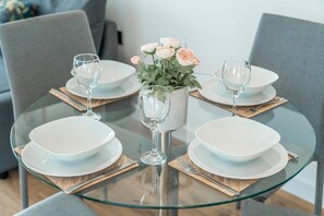 Un tavolo da pranzo con piatti bianchi, bicchieri trasparenti e un vaso con fiori.