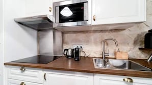 A modern kitchen with a built-in microwave, stainless steel sink, and wooden countertop. - Cocoon Rodier (Paris)