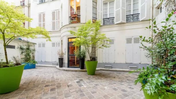 A courtyard with a cobblestone floor, surrounded by white buildings with shutters and balconies. - Cocoon Rodier (Paris)