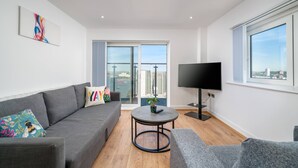 A modern living room with a grey sofa, a round coffee table, a flat-screen TV, and a balcony with a city view.