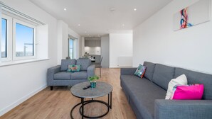 A modern living room with a grey sofa, a round coffee table, and a view of the kitchen in the background.