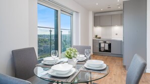 A modern dining area with a glass table, grey chairs, and a view of the city.
