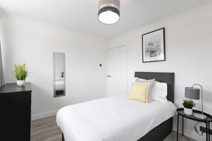 A modern bedroom with a bed, bedside table, lamp, and a potted plant.