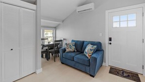 A living room with a blue sofa, white walls, a dining area, and a white door.