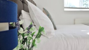 Een slaapkamer met een bed, witte kussens, een blauwe lamp en een raam.