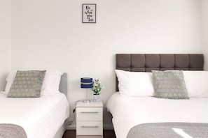 A hotel room with two beds, a bedside table with a lamp and a vase, and a wall with a motivational quote. - Skyvillion - Valley Way - 3bed House In Stevenage (Stevenage)