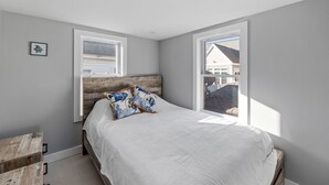 A bedroom with a bed, two windows, a wooden headboard, and a small wooden table. - Winter Beach Refuge for Nurses, Professionals (Hampton)