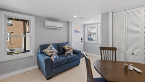 A modern living room with a blue sofa, a dining table, and a white air conditioning unit on the wall. - Winter Beach Refuge for Nurses, Professionals (Hampton)