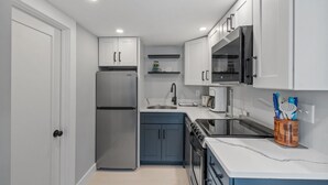 A compact kitchen with white cabinets, a stainless steel refrigerator, a microwave, and a stove. - Winter Beach Refuge for Nurses, Professionals (Hampton)