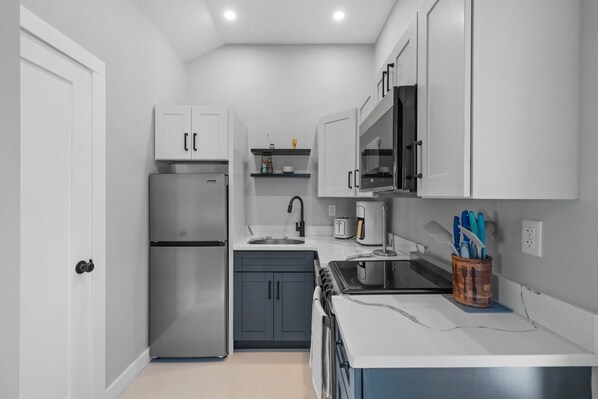 A compact kitchen with a refrigerator, stove, microwave, and sink.