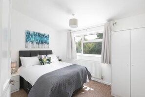 A bedroom with a bed, a window with curtains, a radiator, and a wardrobe.