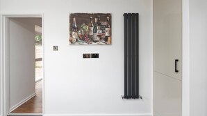 Un pasillo con un cuadro en la pared que representa botellas y frutas, un radiador y una puerta con manija.