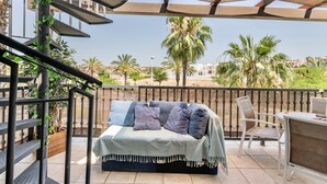 A balcony with a sofa, a table, and chairs, overlooking a palm tree and a building. - Wonderluxury Esuri (Ayamonte)