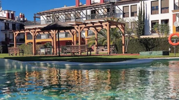 A pool area with a wooden pergola and a lifeguard stand. - Wonderluxury Esuri (Ayamonte)
