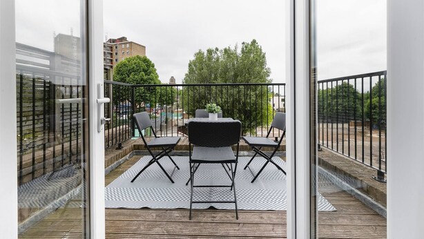 A balcony with a table and chairs, a potted plant, and a view of buildings and trees. - Skyvillion - Central Ldn 3bed Flat Ladbroke Grove (London)