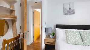 A bedroom with a bed, bedside table, lamp, and a painting of a cityscape. - Skyvillion - Central Ldn 3bed Flat Ladbroke Grove (London)