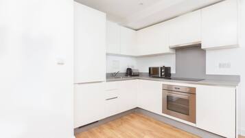 A modern kitchen with white cabinets, a stainless steel oven, and a black coffee maker.