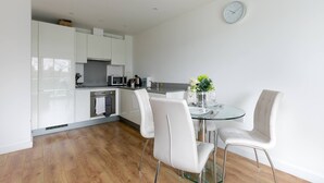 A modern kitchen with white cabinets, a microwave, and a glass dining table with white chairs.