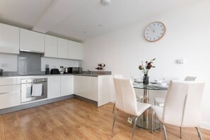 A modern kitchen with white cabinets, stainless steel appliances, and a dining area with a glass table and white chairs.