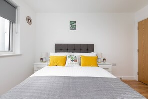 A bedroom with a bed, two bedside tables, a window, a door, and a wall-mounted artwork.