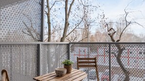 A balcony with a wooden table and chairs, a potted plant, and a view of bare trees. - Stylish Apartment | Balcony and Private Parking (Kraków)